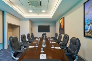 A conference room with a long table, chairs, a projector screen, and artwork on the walls.
