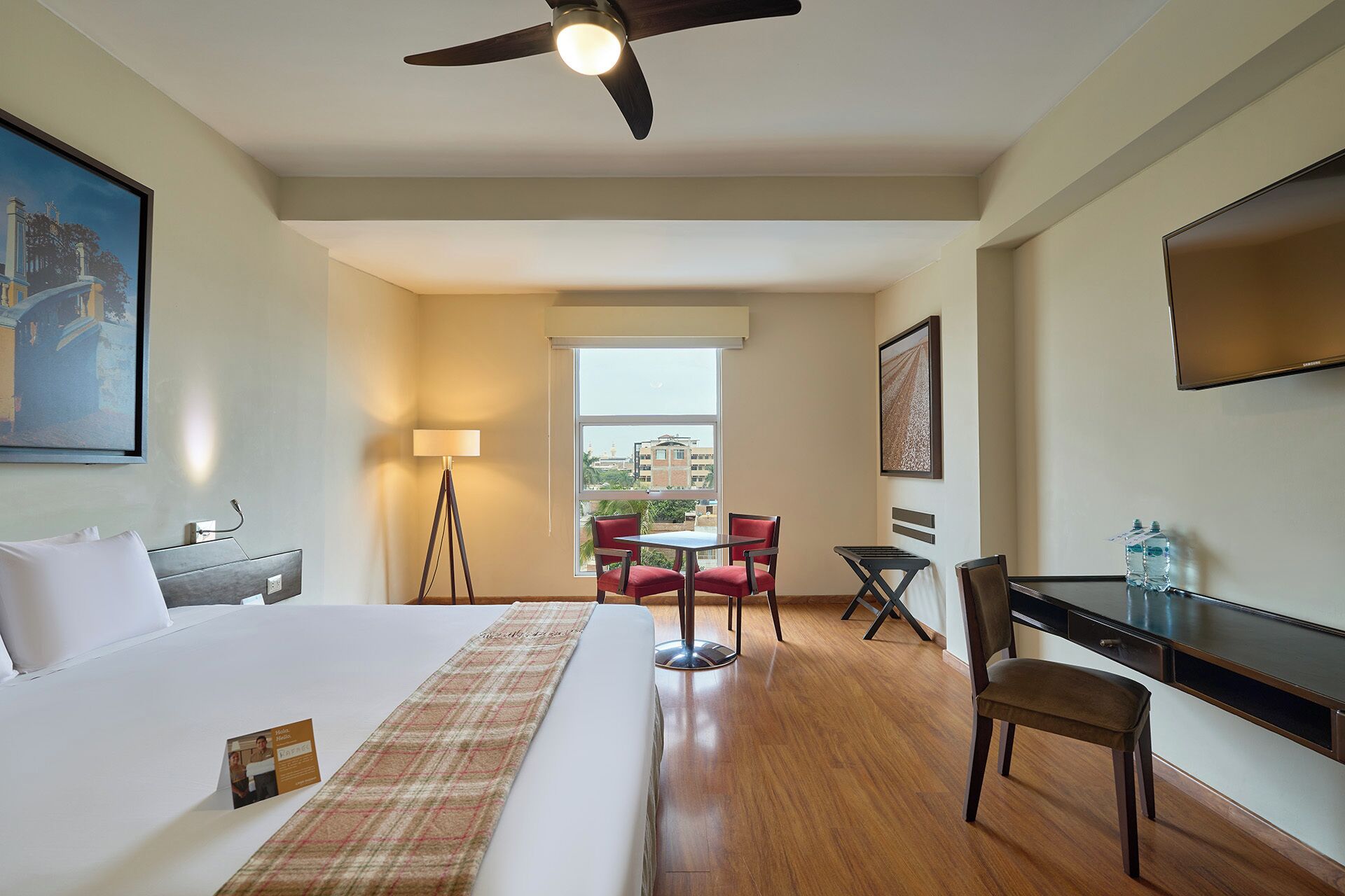 Una habitación de hotel con cama, escritorio, silla, mesa, lámpara y televisor.