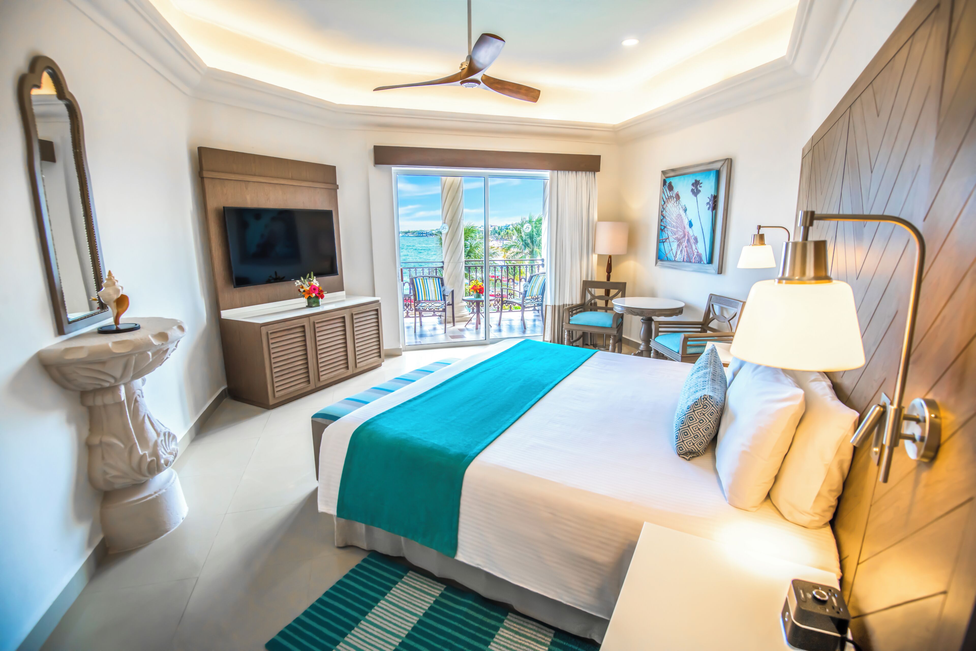 Una habitación de hotel con cama, televisión, balcón y ventilador de techo.