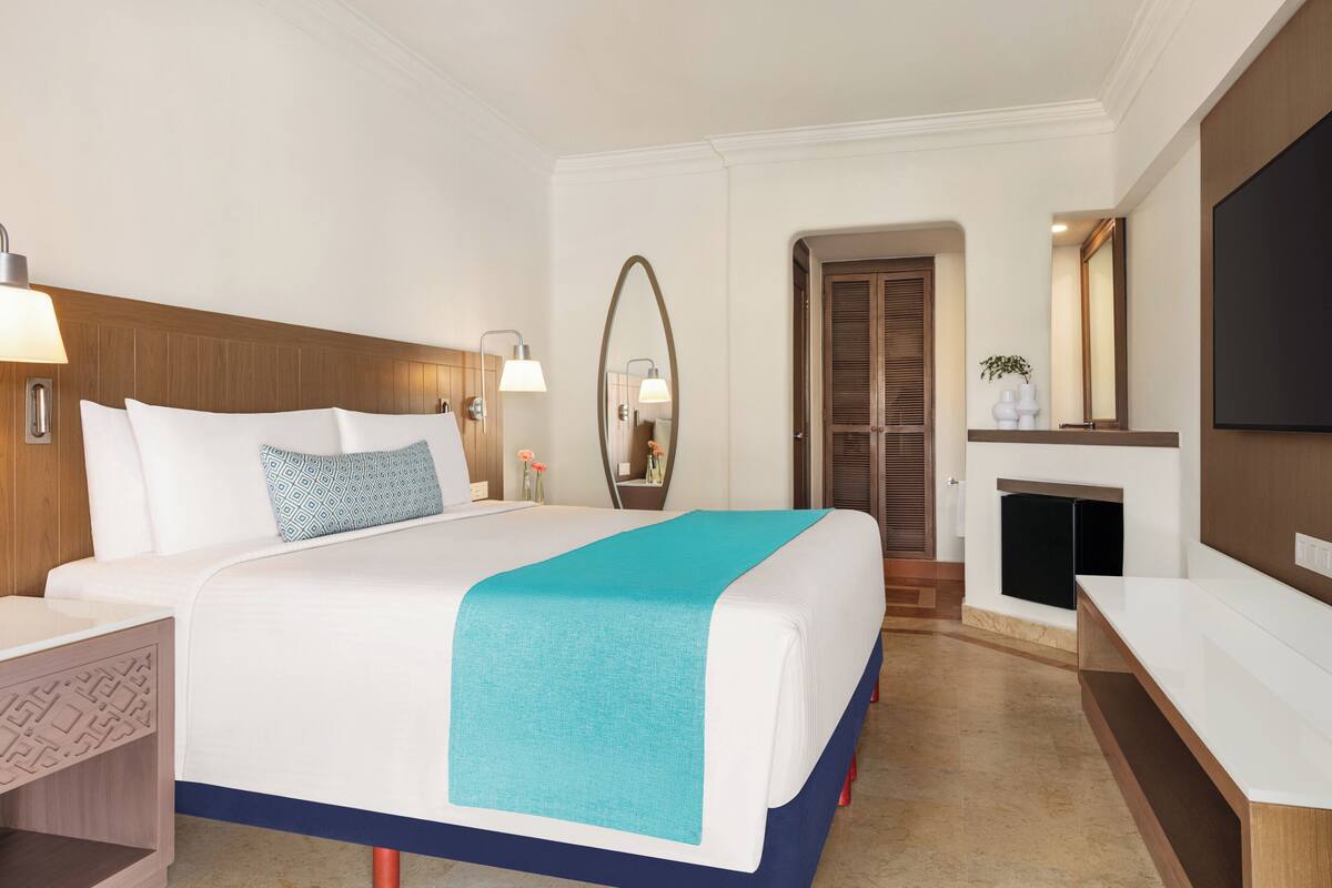 Una habitación de hotel con cama, mesitas de noche, televisor, espejo y chimenea.