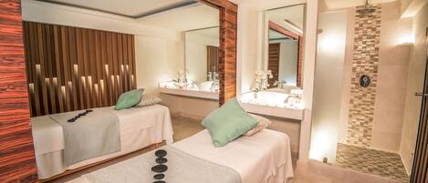A hotel room with two beds, a large mirror, a shower area, and a wooden panel wall.