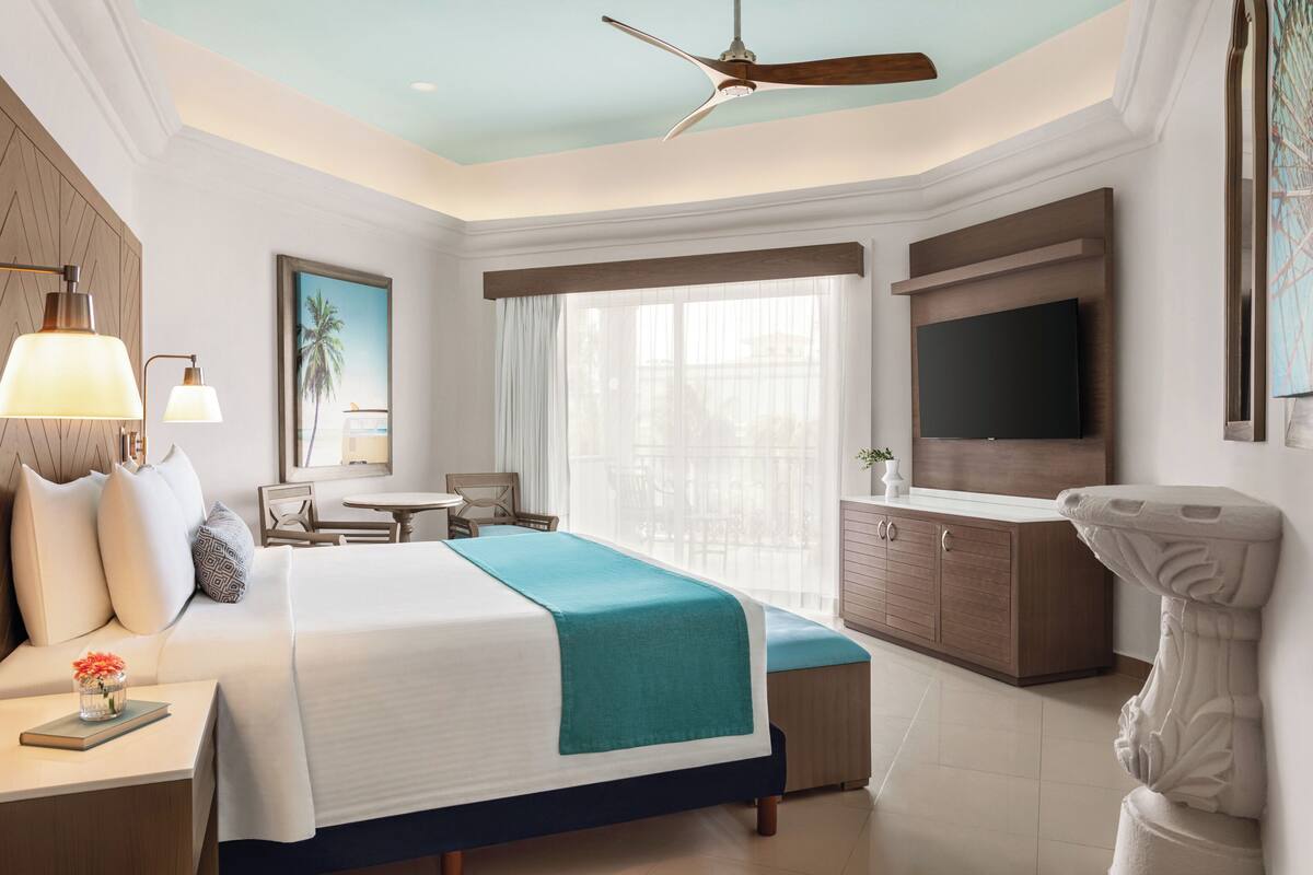 Una habitación de hotel con cama, mesita de noche, lámpara, televisor y ventilador de techo.