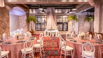 Een balzaal met een centrale tafel waarop het woord 'LOVE' staat, omringd door witte stoelen en tafels met servies.
