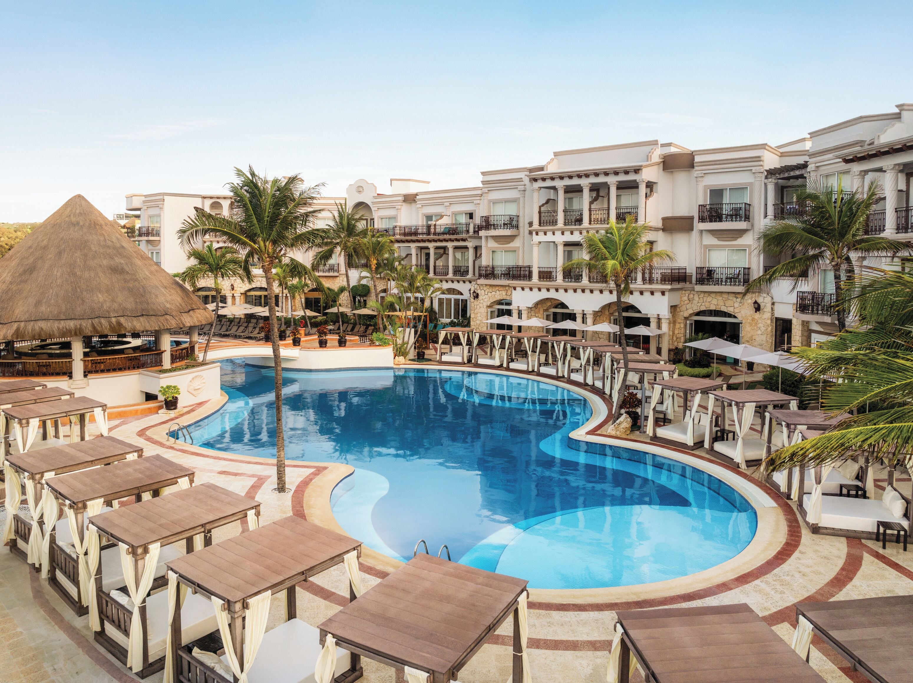 A resort pool area with a large pool, lounge chairs, and a bar area with a thatched roof.