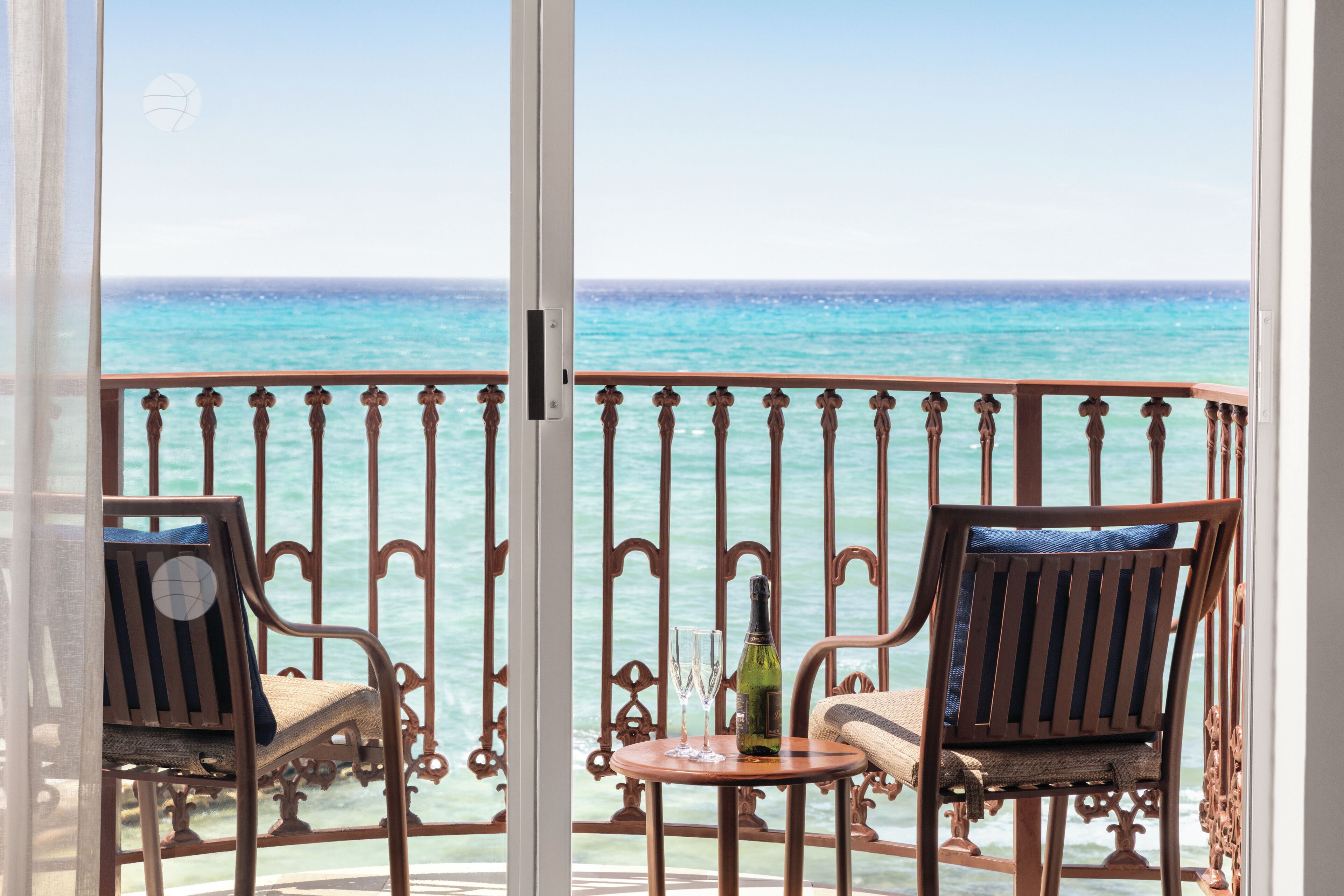 A balcony with two wooden chairs, a small table, and a bottle of wine.