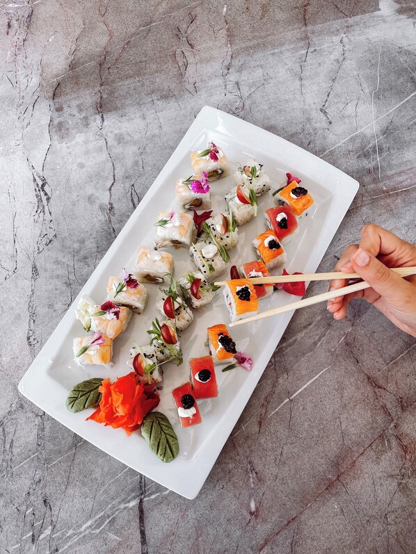 Un plato rectangular blanco con rollos de sushi y adornos.