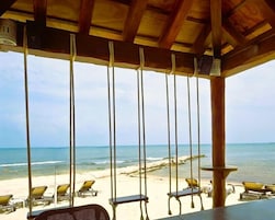 Vista de la playa desde una estructura de madera con columpios, sillas de descanso y un cielo despejado.