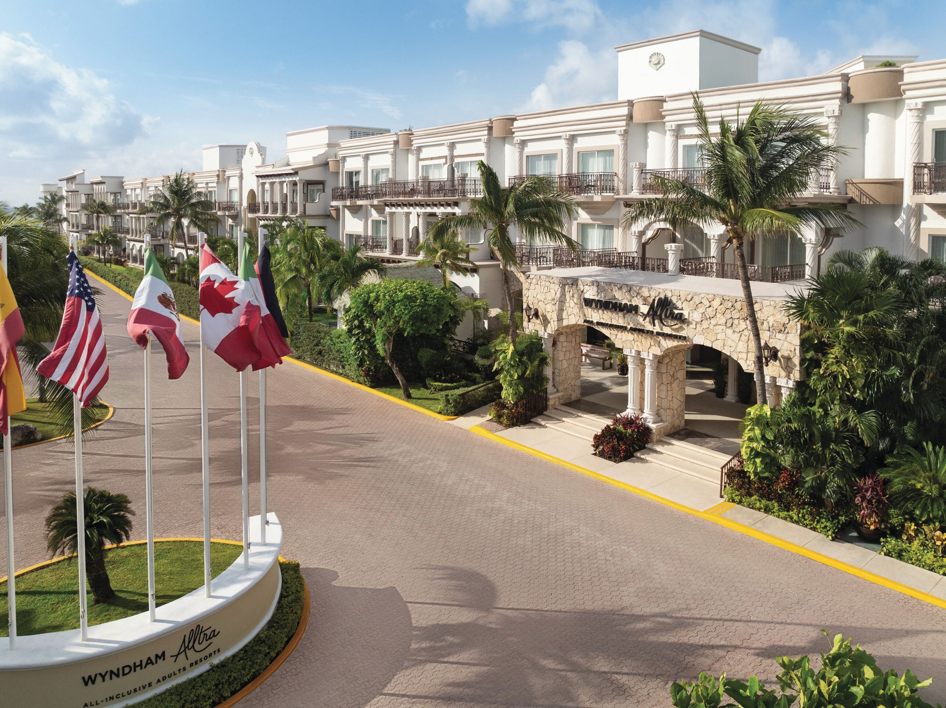 Wyndham Allura Resort with a stone bridge, palm trees, and flags.