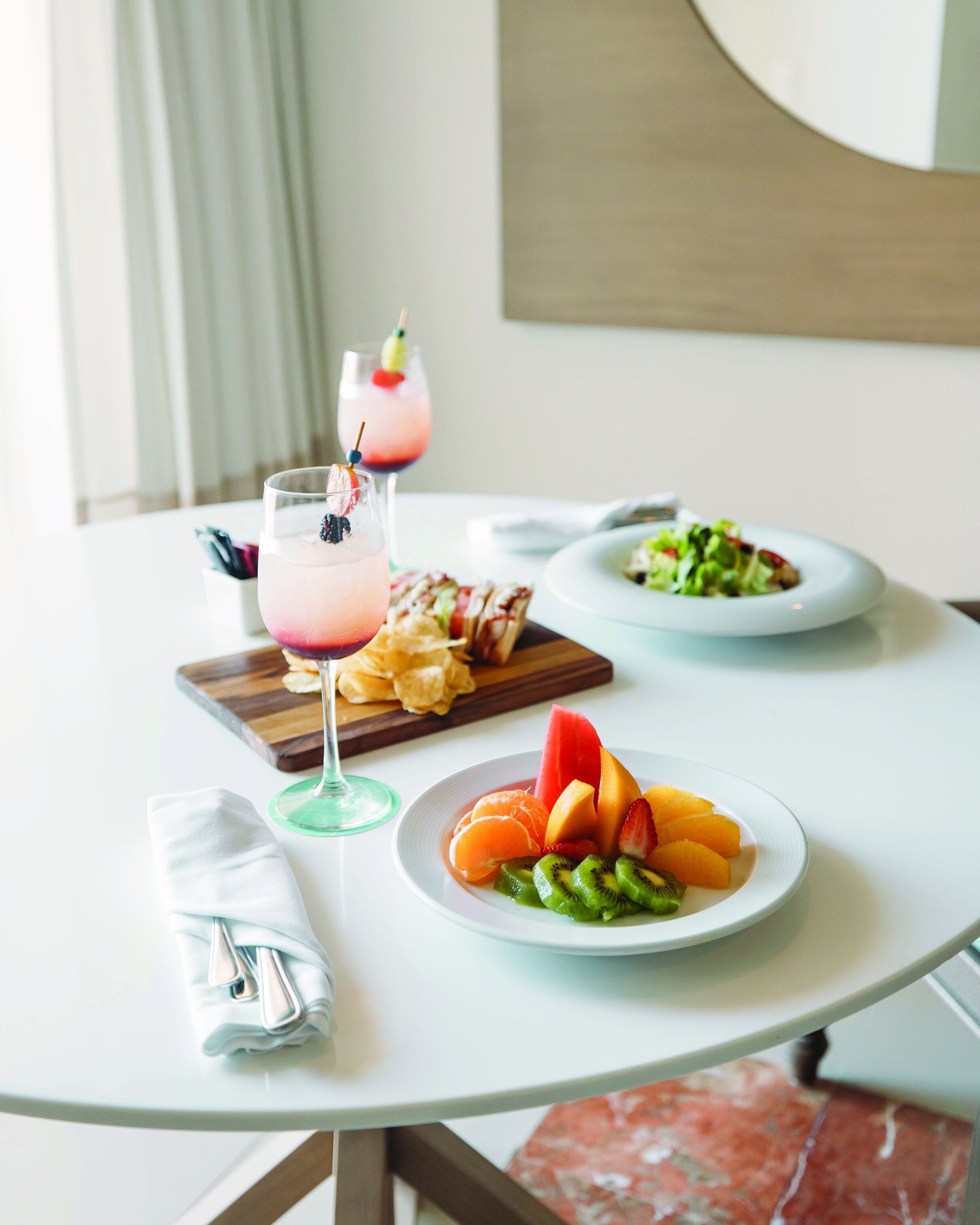 Une table avec une assiette de fruits, un verre d’une boisson rose et une assiette de salade.