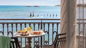 Une table avec des aliments pour le petit-déjeuner et un verre de jus d’orange, le tout placé sur un balcon donnant sur la mer.