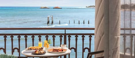 Ein Tisch mit Frühstücksleckereien und einem Glas Orangensaft auf einem Balkon mit Blick auf das Meer.