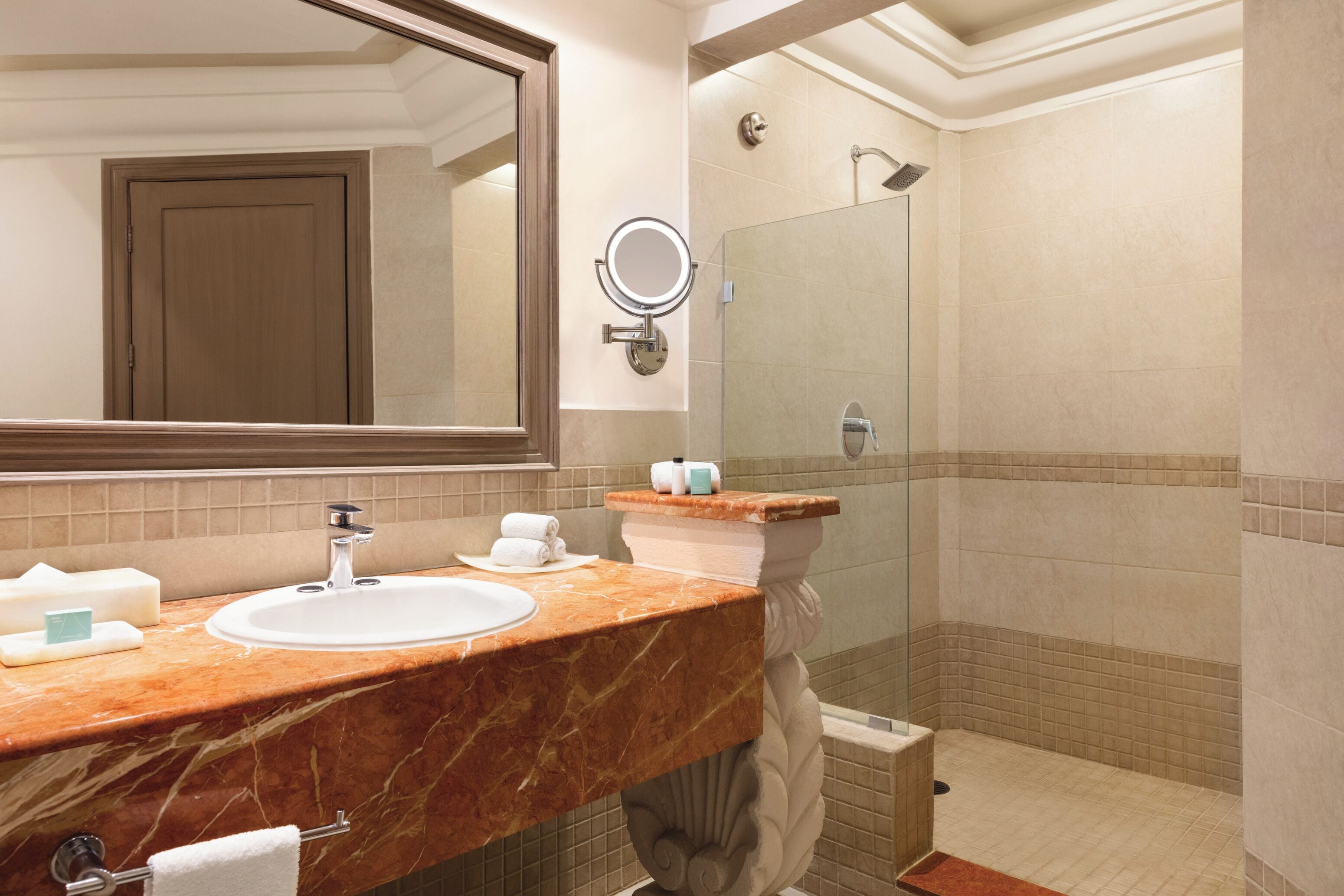 Une salle de bain avec un lavabo en marbre, un grand miroir, une douche et un porte-serviettes.