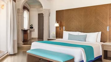 Habitación de hotel con una cama grande, cabecero de madera, un banco y una mesita de noche con lámpara.