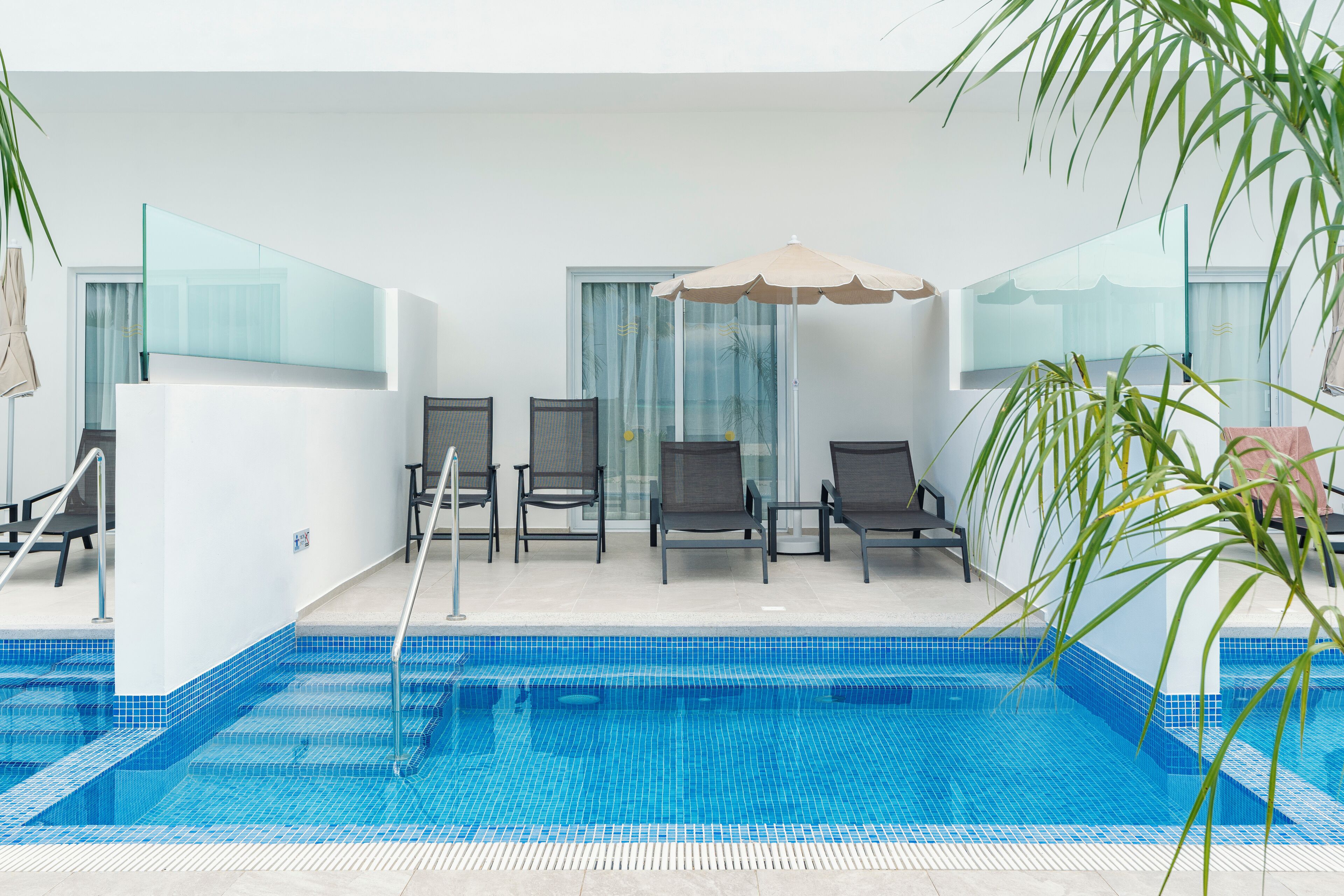 Un área de piscina con barandilla de cristal, sillas de descanso y una sombrilla grande.
