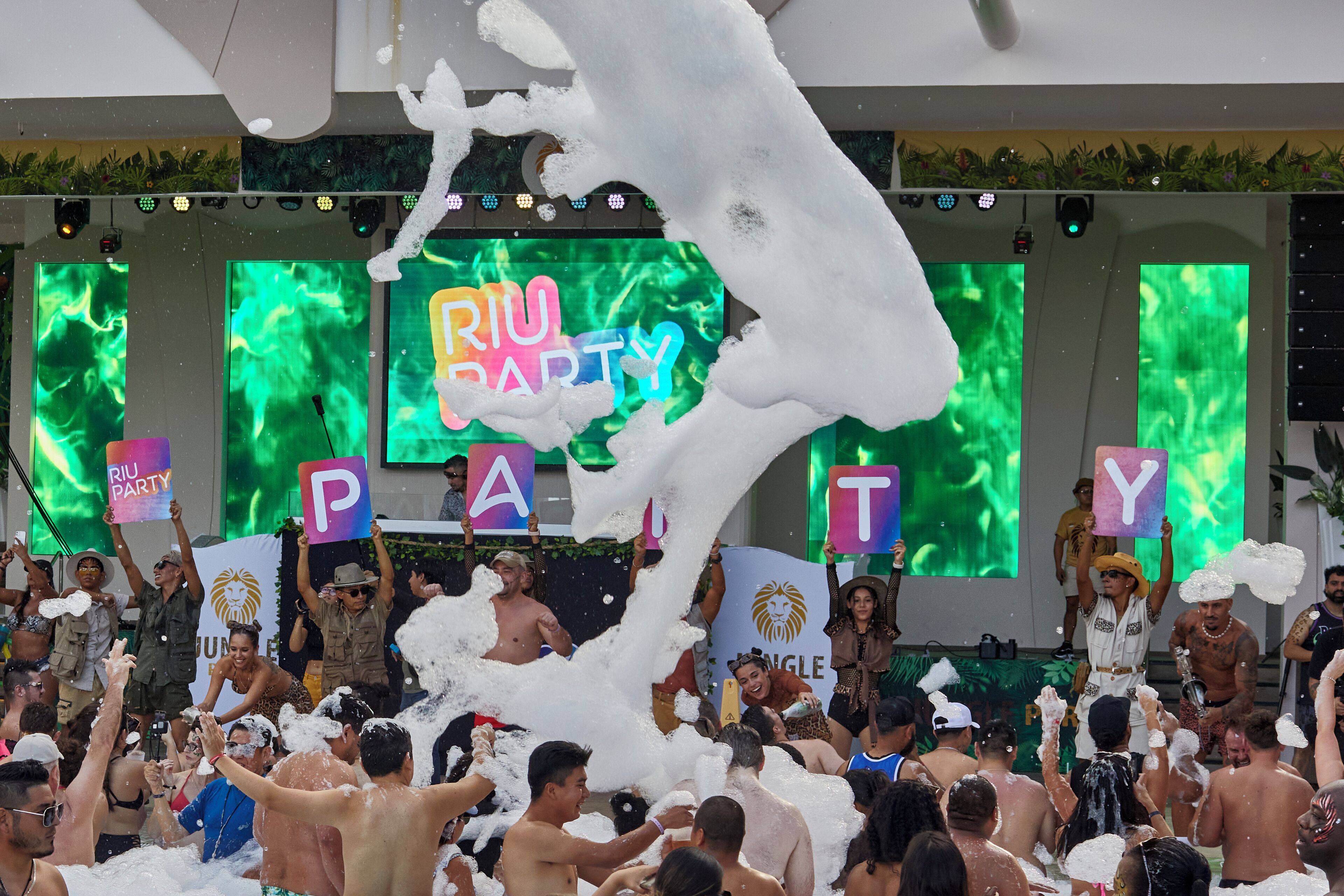 A crowded indoor event with a stage and a banner reading "Riu Party".