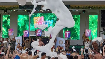 A crowded indoor event with a stage and a banner reading "Riu Party".