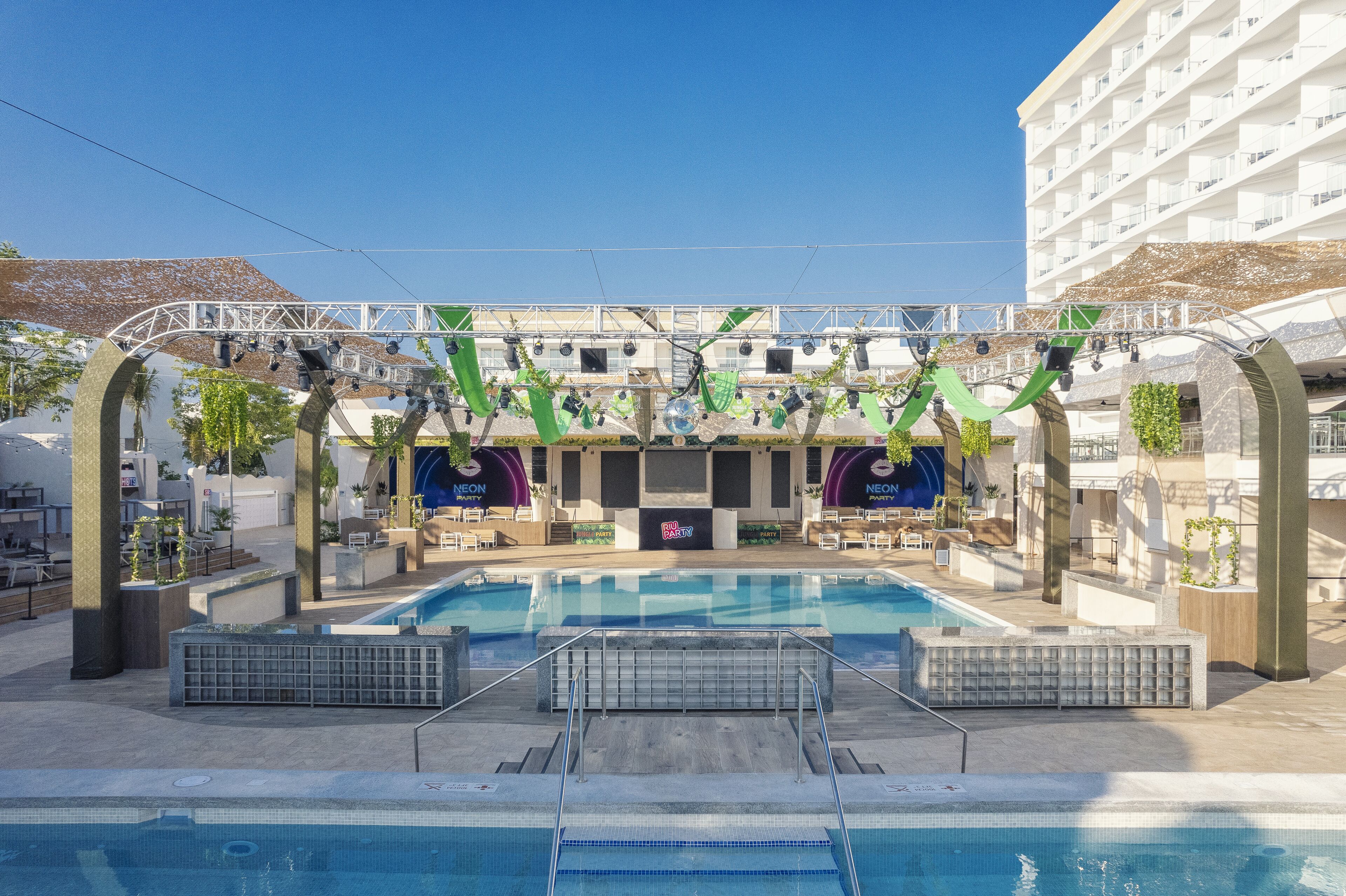 A pool area with a clear view of the pool, steps leading into the water, and a covered seating area with a neon sign.