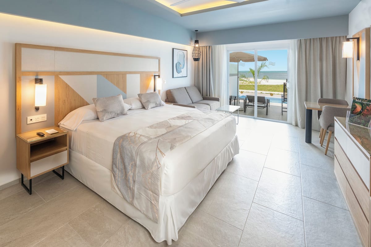 Una habitación de hotel moderna con una cama grande, un escritorio y un balcón con vistas a la playa.