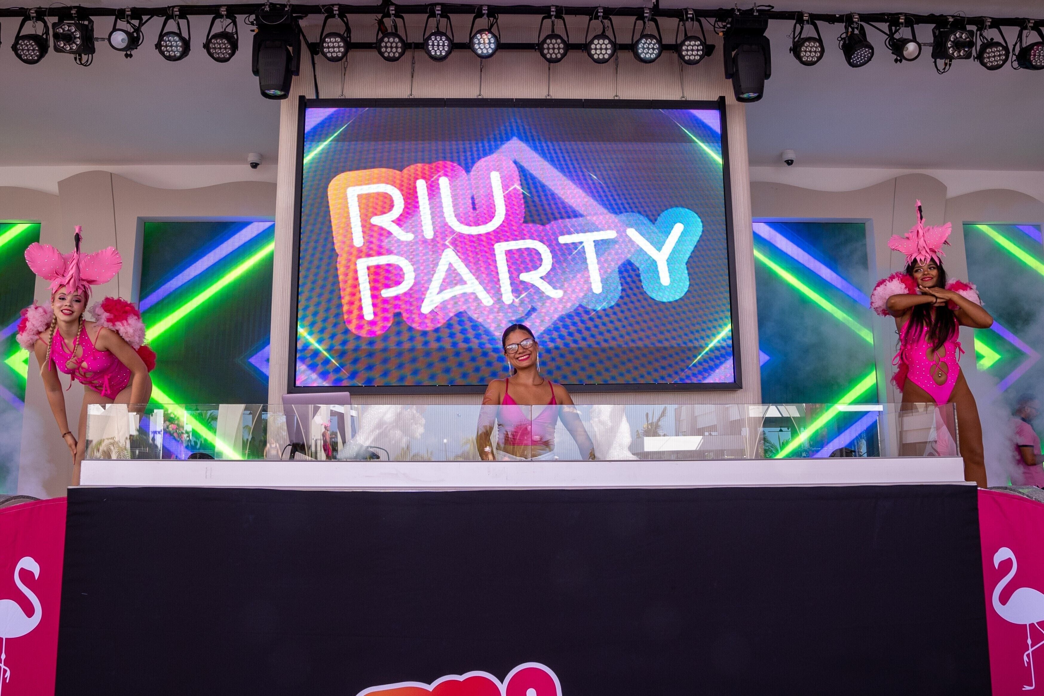 A stage with a large screen displaying "RIU PARTY" and performers in pink costumes.