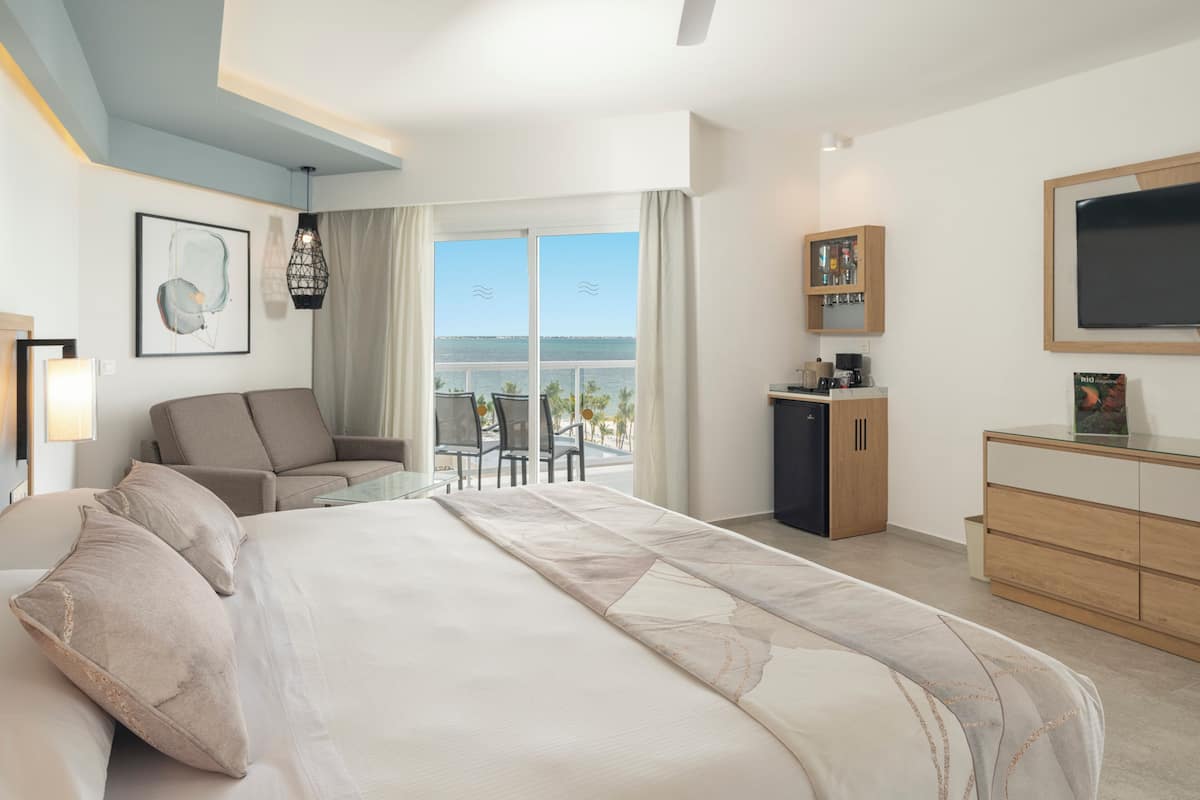 Una habitación de hotel moderna con una cama grande, un sofá, un escritorio y vista al océano.