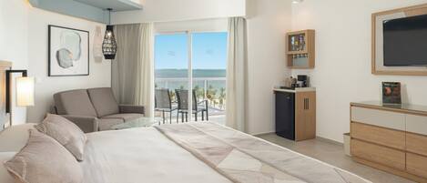 A modern hotel room with a large bed, a sofa, a desk, and a view of the ocean.