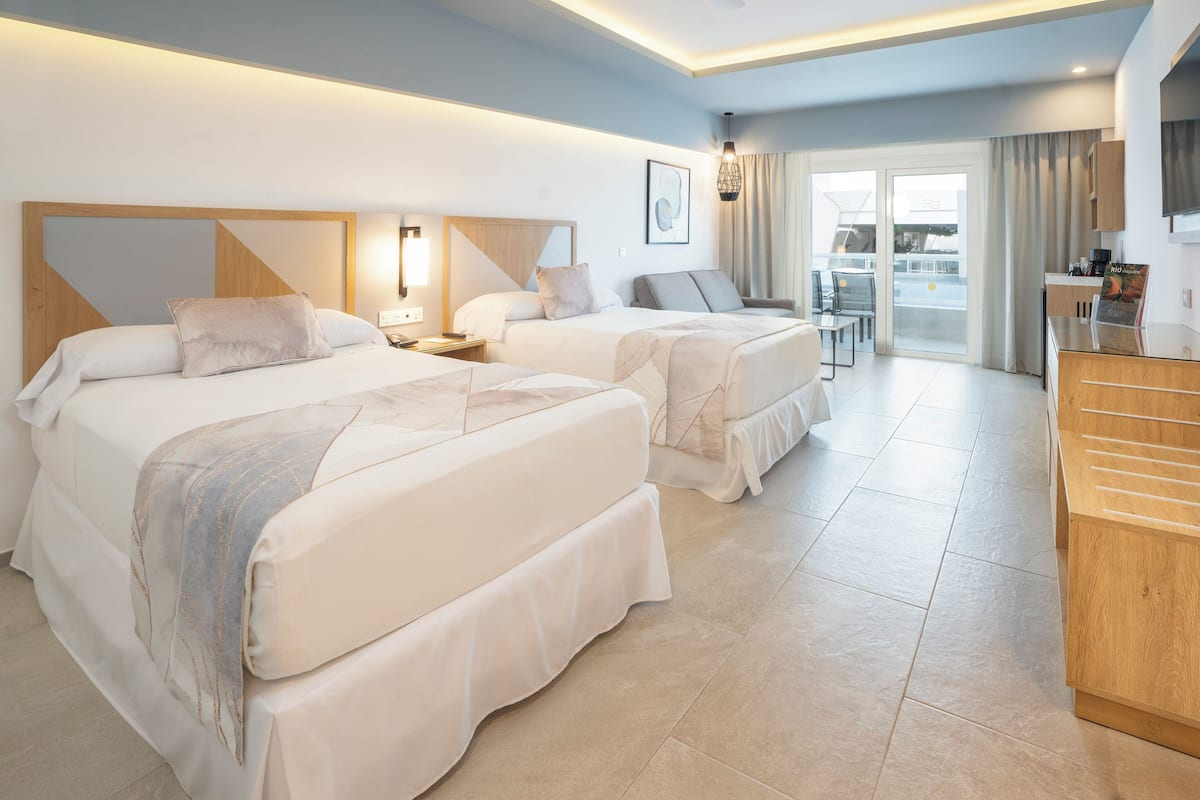 Habitación de hotel con dos camas, un escritorio y vistas al exterior.