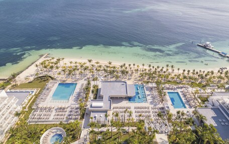 An aerial view of a resort with multiple swimming pools, a beach, and a pier.