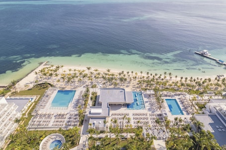 An aerial view of a resort with multiple swimming pools, a beach, and a pier.