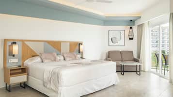 A modern hotel room with a large bed, a chair, a small table, and a balcony with a view.