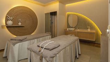 Relax in a serene spa room with two massage tables, a large mirror, and a wooden vanity.