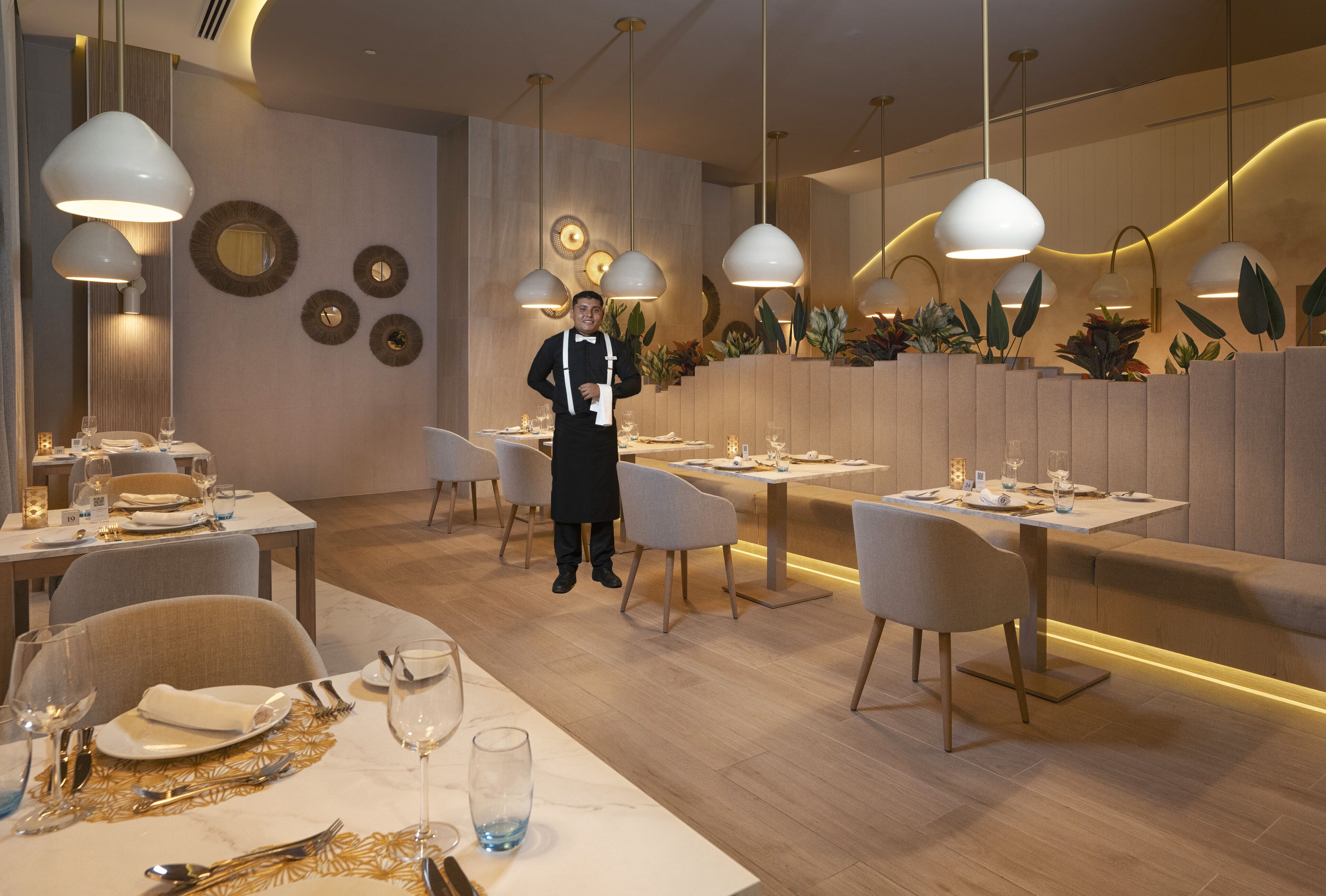 Un interior de restaurante moderno con varias mesas, sillas e iluminación colgante.