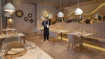 Un interior de restaurante moderno con varias mesas, sillas e iluminación colgante.