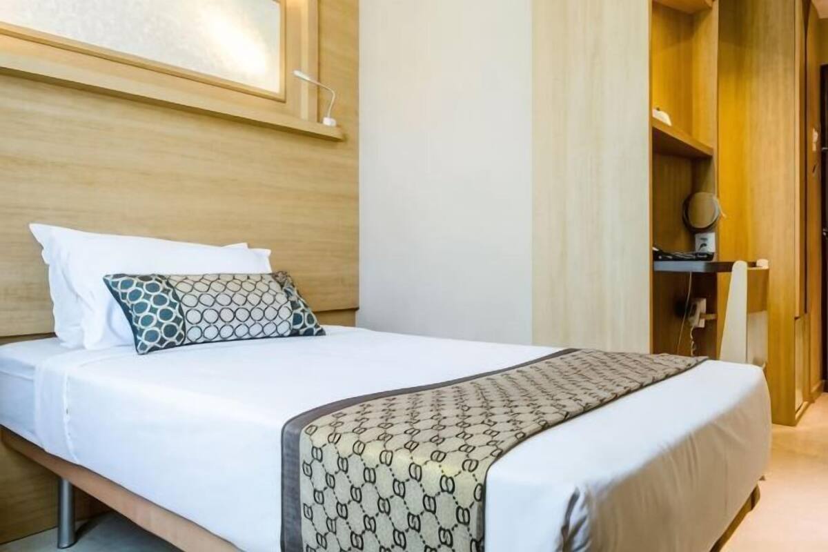A neatly made bed with a patterned throw, a bedside table with a lamp, and a wooden headboard.