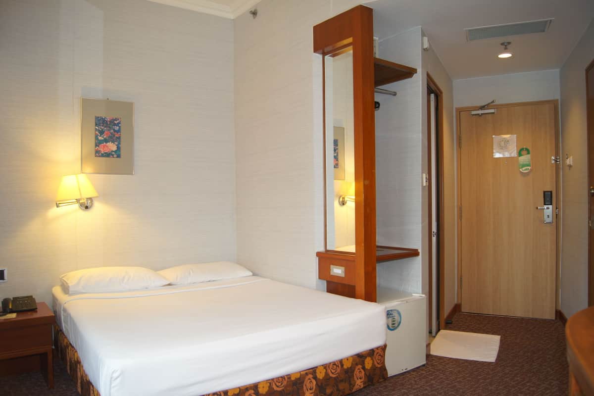 A hotel room with a bed, a bedside table, a lamp, a mirror, and a door.