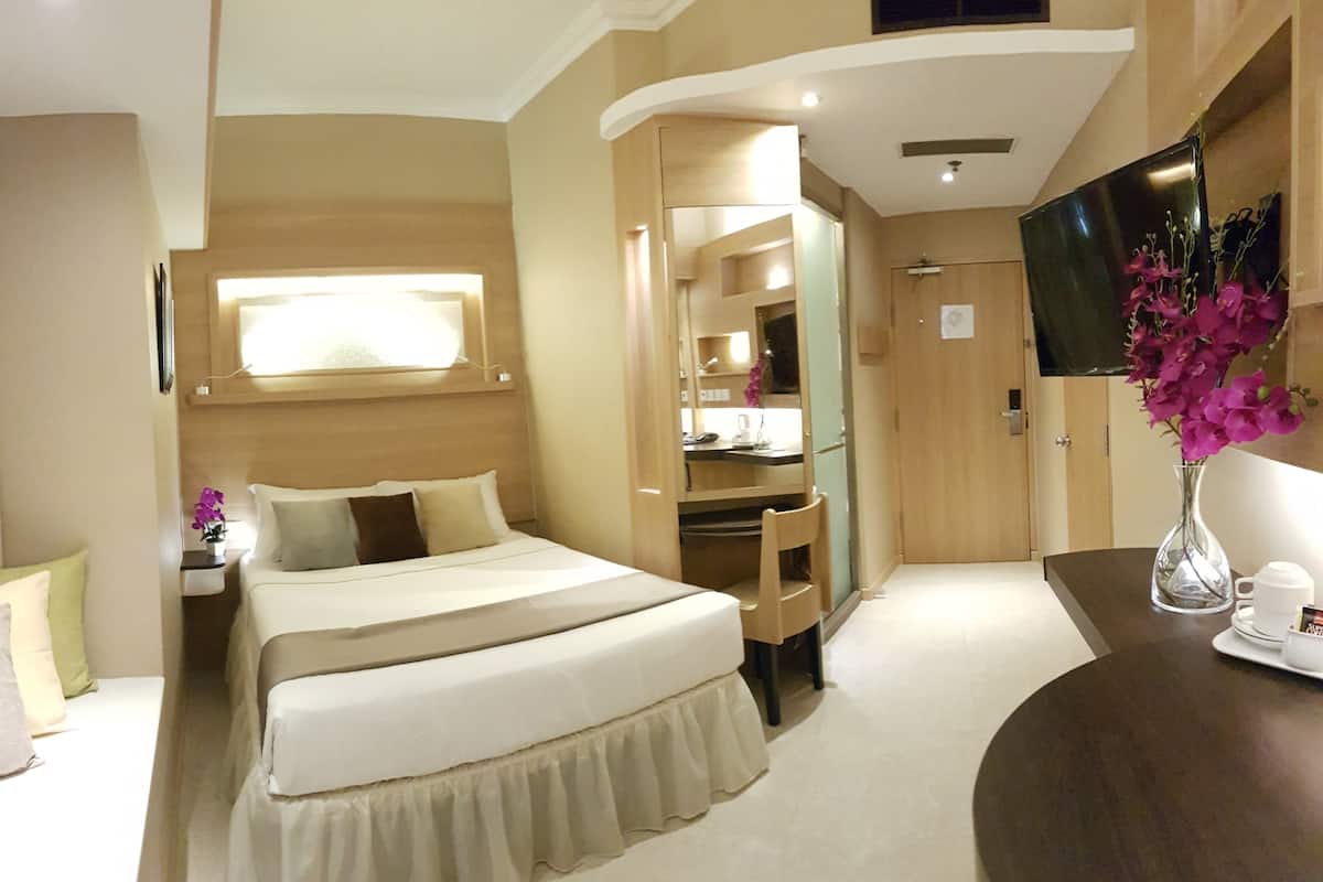 A hotel room with a bed, a desk, a TV, and a vase with flowers.
