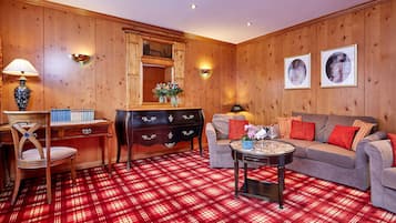 A room with a plaid carpet, wooden walls, a sofa, a coffee table, a desk, and a lamp.