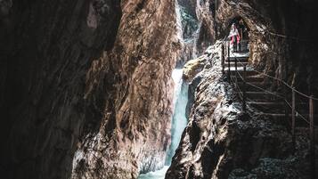 A person standing on a wooden staircase leading to a waterfall in a rocky canyon.