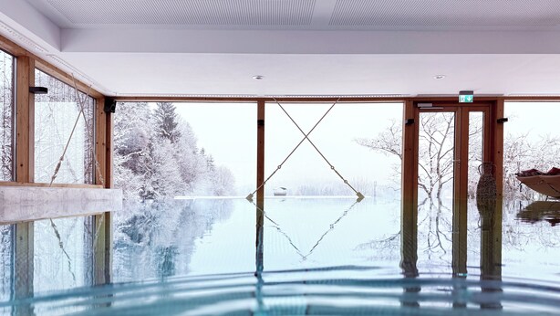 A glass-enclosed indoor pool with a view of a snowy landscape. - Romantik Alpenhotel Waxenstein (Grainau)