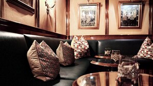 A dark leather booth with patterned cushions, framed pictures on the wall, and a glass vase on a table. - Romantik Alpenhotel Waxenstein (Grainau)