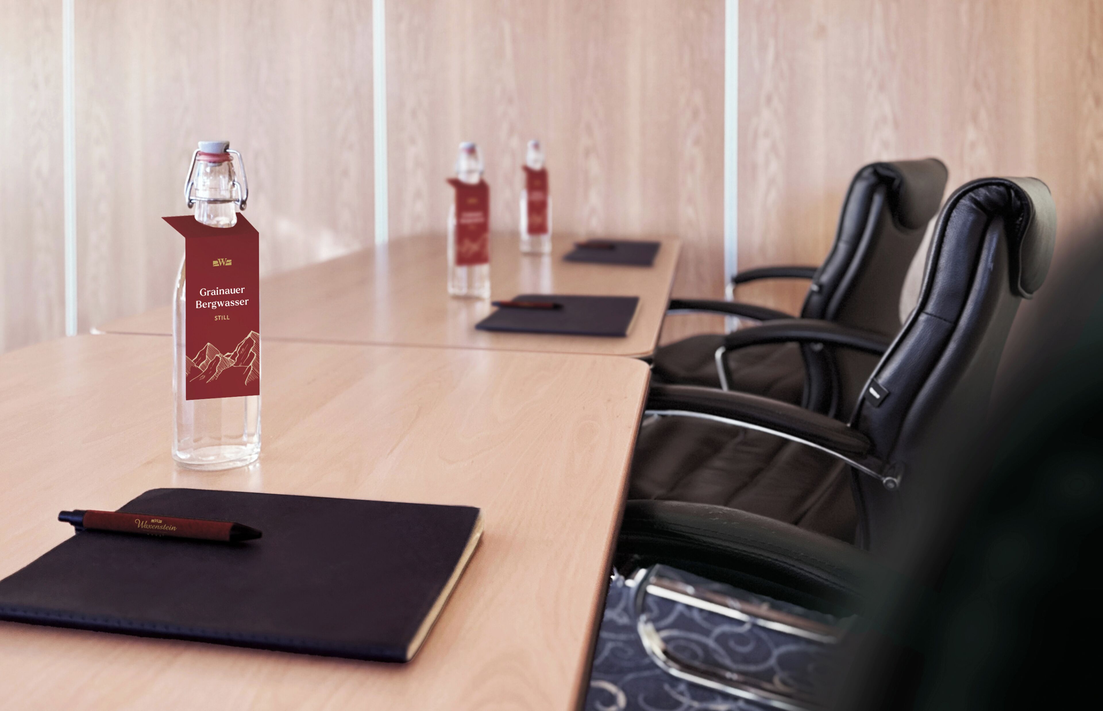 A conference table with a bottle of Grainauer Bergwässer Still, two water bottles, a notebook, and a pen.