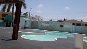 Una piscina en la azotea de diseño curvo, rodeada por un muro bajo y una estructura de pérgola.