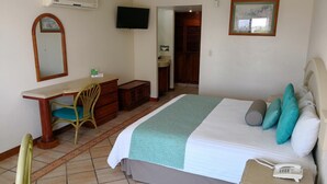 Habitación de hotel con cama, escritorio con silla, televisión y baño visible a través de una puerta abierta.