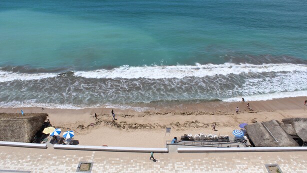Vista de la playa con piscina, sombrillas y sillas.