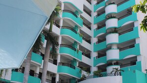 Un hotel con varios balcones, piscina y mobiliario exterior con sombrillas.