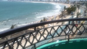 Vista desde un balcón con vista a una playa y un horizonte urbano de fondo.