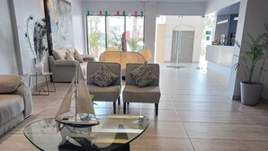 A modern living room with a glass coffee table, two armchairs, a sofa, and a potted plant.