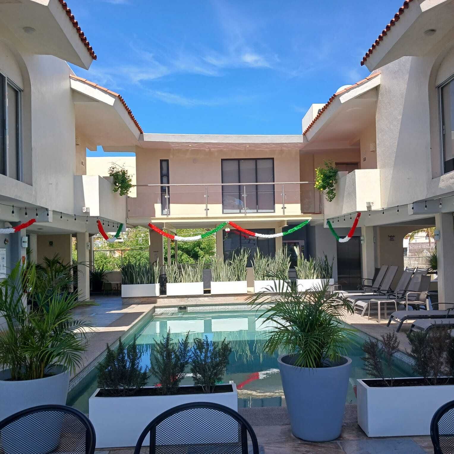 Une piscine entourée de bâtiments dotés de balcons et de coins salons extérieurs, avec un ciel bleu dégagé au-dessus.