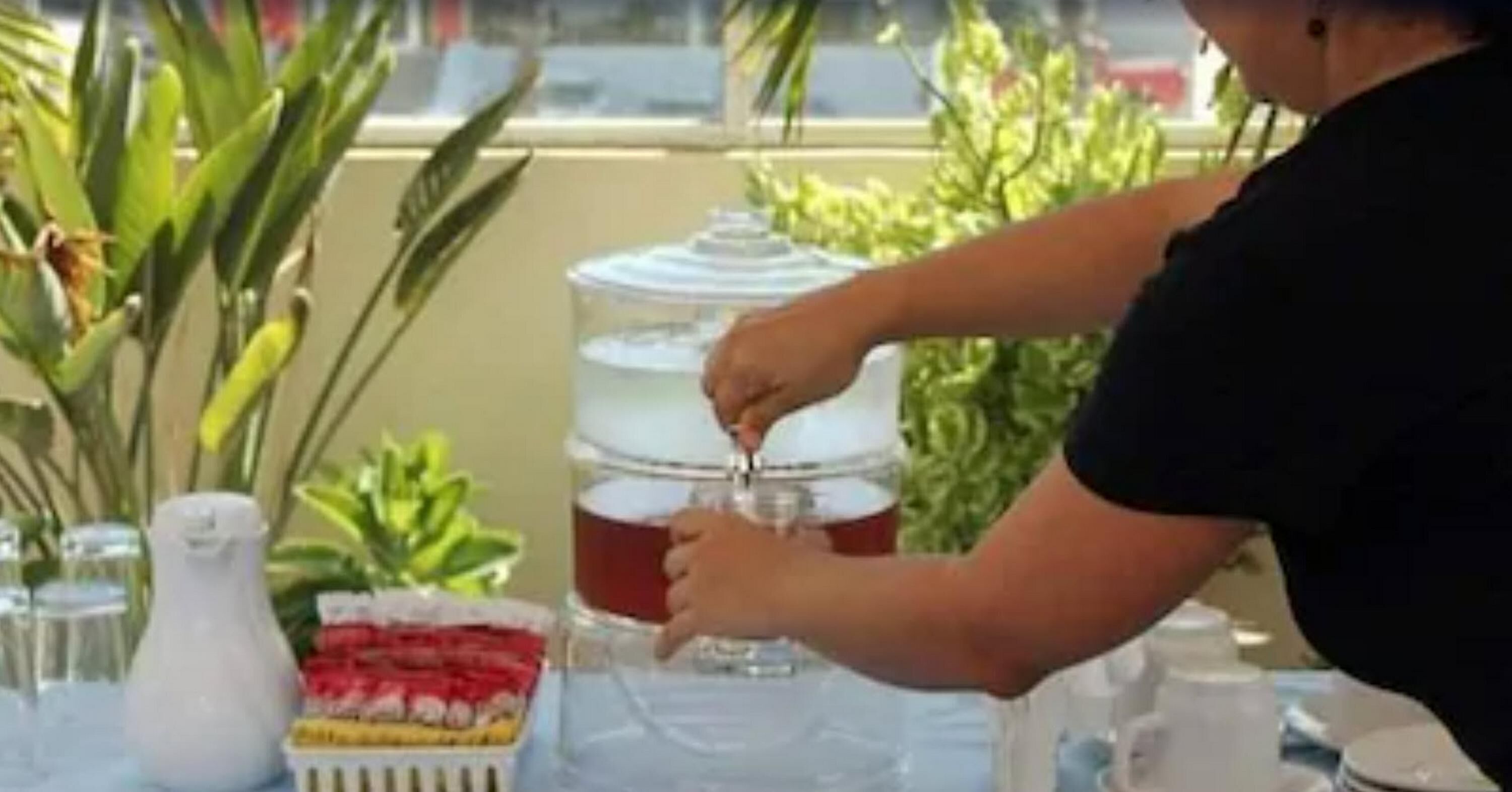 A person pouring a beverage from a large container into a glass.