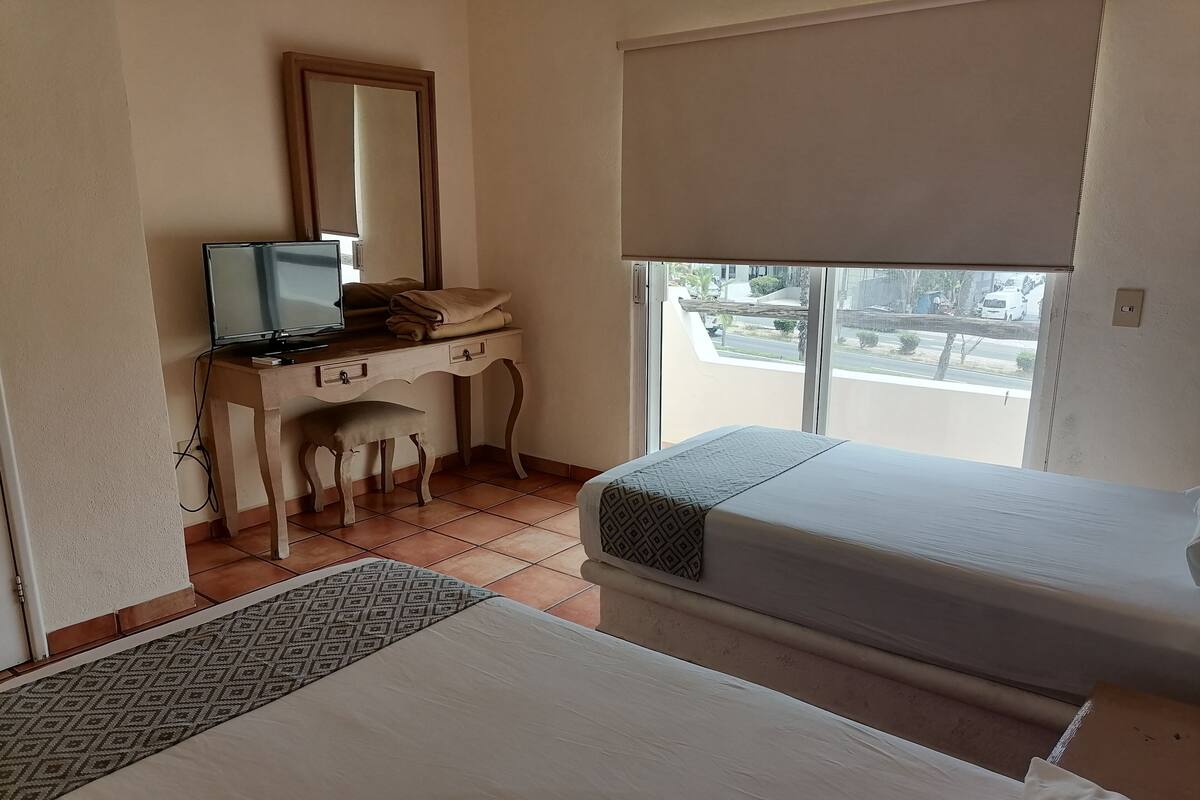 Habitación de hotel con una cama, un escritorio con computadora, una silla y una ventana con vista al exterior.