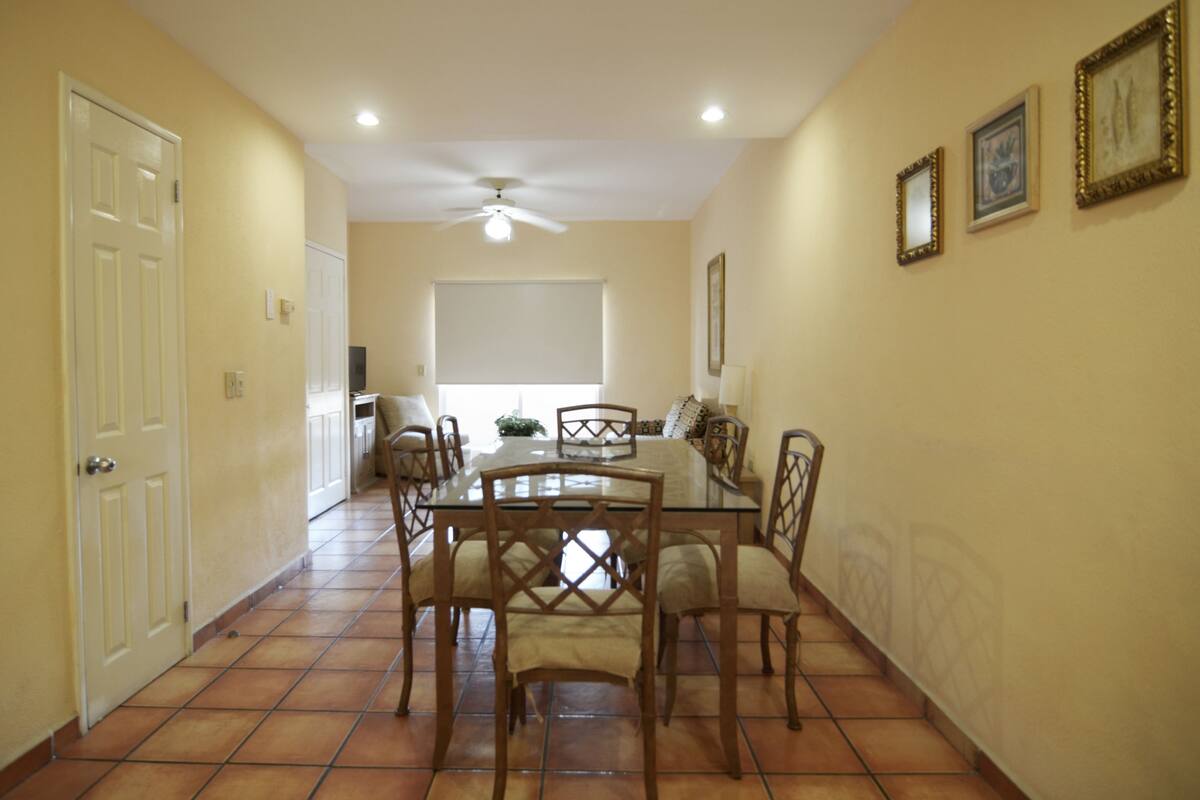 Un comedor con mesa de vidrio, sillas de madera y ventilador de techo.